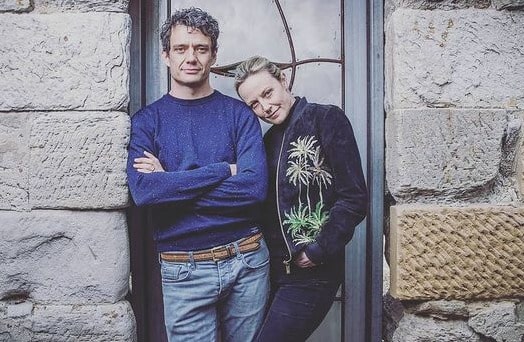 Marta Dusseldrop posing with her husband by wearing black pant and black pullover.